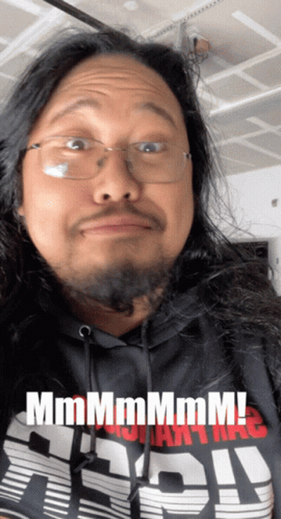 A Man With Long Hair And Glasses Is Wearing A Shirt That Says " Mmmmm " GIF
