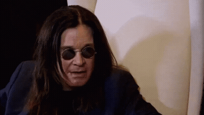 A Man With Long Hair And Sunglasses Is Sitting In A Chair . GIF
