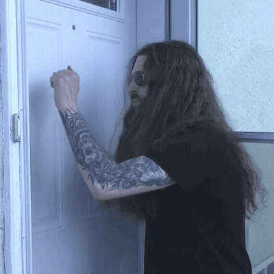 A Man With Long Hair And Tattoos Knocks On A Door GIF