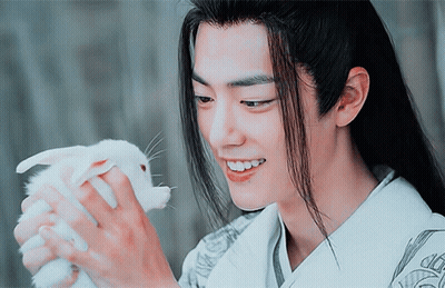 A Man With Long Hair Holds A Small White Rabbit In His Hands GIF
