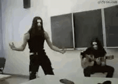 A Man With Long Hair Is Dancing In Front Of A Blackboard In A Classroom While Another Man Plays A Guitar . GIF