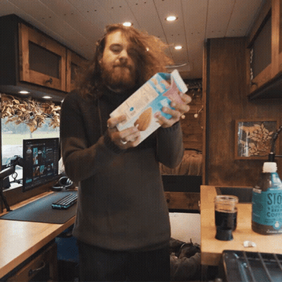 A Man With Long Hair Is Holding A Box Of Cookies In His Hands GIF