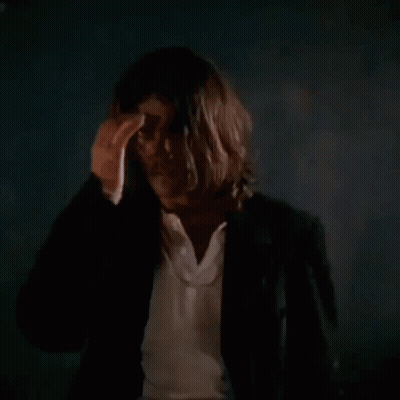 A Man With Long Hair Is Holding A Gun In His Hand GIF