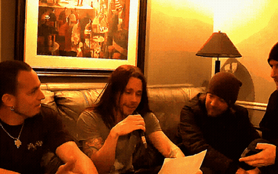 A Man With Long Hair Is Holding A Microphone And Talking To Another Man GIF