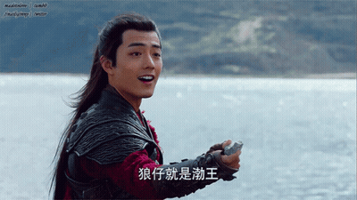 A Man With Long Hair Is Holding A Rock In Front Of A Body Of Water And Has Chinese Writing On His Arm GIF