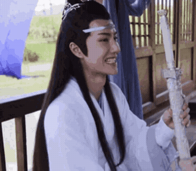 A Man With Long Hair Is Holding A Sword And Smiling While Sitting On A Balcony . GIF