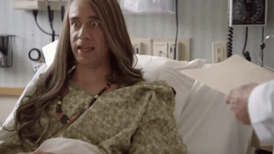 A Man With Long Hair Is Laying In A Hospital Bed With A Doctor . GIF