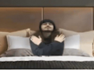 A Man With Long Hair Is Laying On A Bed With His Hands Folded . GIF