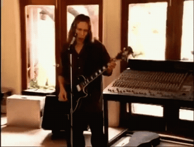 A Man With Long Hair Is Playing A Guitar And Singing Into A Microphone . GIF