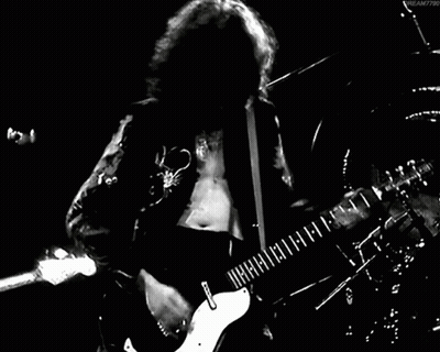 A Man With Long Hair Is Playing A Guitar In A Black And White Photo . GIF