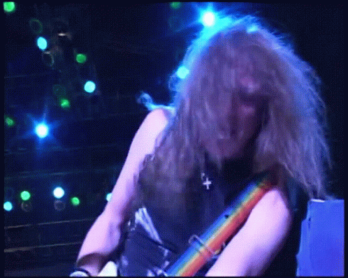 A Man With Long Hair Is Playing A Guitar In A Dark Room With Blue Lights Behind Him GIF
