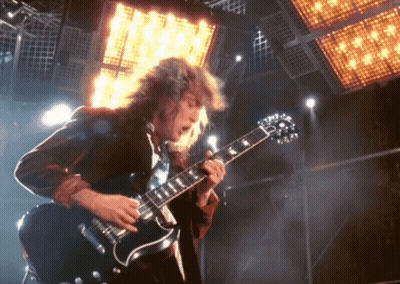 A Man With Long Hair Is Playing A Guitar In Front Of A Large Light GIF