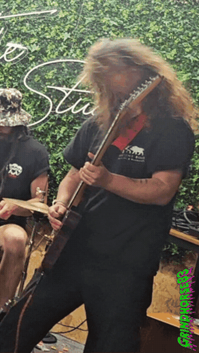 A Man With Long Hair Is Playing A Guitar In Front Of A Sign That Says Stu GIF