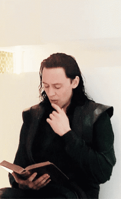 A Man With Long Hair Is Reading A Book While Sitting Down GIF