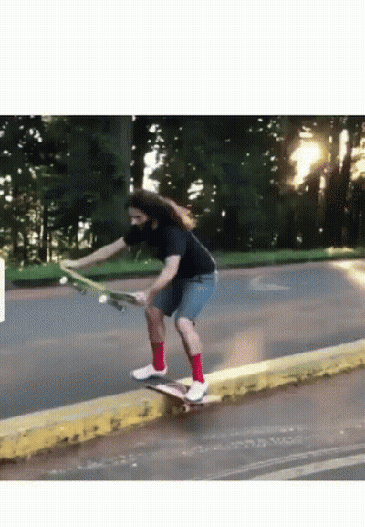 A Man With Long Hair Is Riding A Skateboard Down A Street GIF