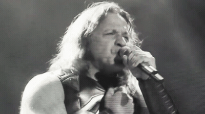 A Man With Long Hair Is Singing Into A Microphone In A Black And White Photo GIF