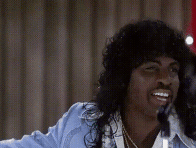 A Man With Long Hair Is Singing Into A Microphone While Wearing A Blue Jacket . GIF