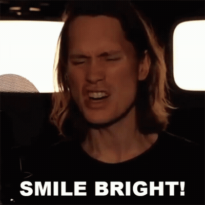 A Man With Long Hair Is Singing Into A Microphone With The Words Smile Bright Behind Him GIF