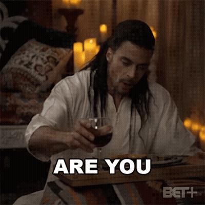 A Man With Long Hair Is Sitting At A Table With A Glass Of Wine And Says " Are You " GIF