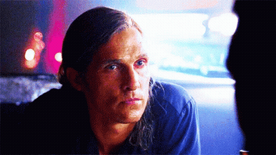 A Man With Long Hair Is Sitting In A Dark Room Looking At Something GIF