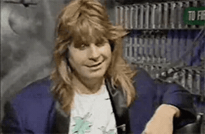 A Man With Long Hair Is Sitting On A Couch Smiling . GIF
