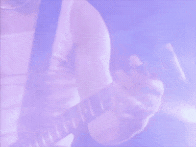 A Man With Long Hair Is Smiling And Looking At The Camera While Playing A Guitar . GIF