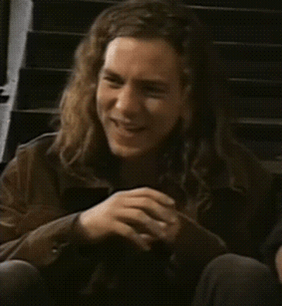 A Man With Long Hair Is Smiling And Sitting On A Set Of Stairs GIF