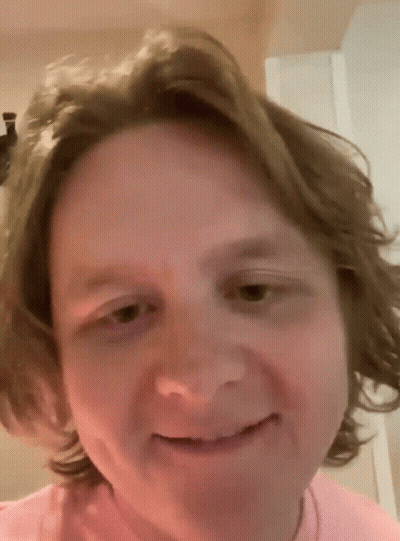 A Man With Long Hair Is Smiling And Wearing A Pink Shirt GIF