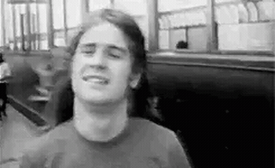 A Man With Long Hair Is Smiling In A Black And White Photo While Sitting In A Restaurant . GIF