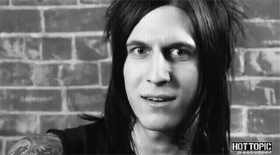 A Man With Long Hair Is Standing In Front Of A Brick Wall And Smiling . GIF
