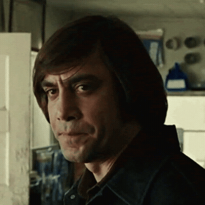 A Man With Long Hair Is Standing In Front Of A Door And Making A Funny Face . GIF