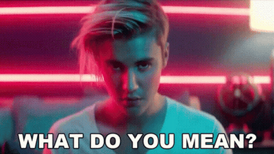 A Man With Long Hair Is Standing In Front Of A Neon Sign And Says What Do You Mean . GIF