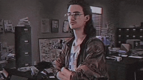 A Man With Long Hair Is Standing In Front Of A Sign That Says Hackerman GIF