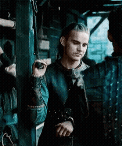 A Man With Long Hair Is Standing Next To A Wall Holding A Rope . GIF