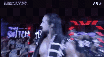 A Man With Long Hair Is Walking On A Stage In Front Of A Crowd Of People . GIF