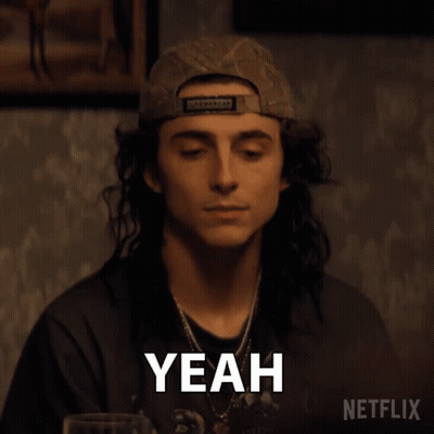 A Man With Long Hair Is Wearing A Baseball Cap And Making A Yeah Gesture . GIF