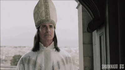 A Man With Long Hair Is Wearing A Bishop 'S Hat And Robe . GIF