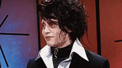 A Man With Long Hair Is Wearing A Black Suit And A White Collar . GIF
