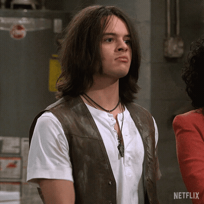 A Man With Long Hair Is Wearing A Brown Vest And A White Shirt With A Netflix Logo On The Bottom GIF