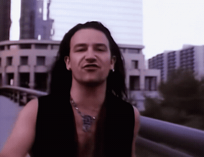 A Man With Long Hair Is Wearing A Necklace With A Cross On It GIF