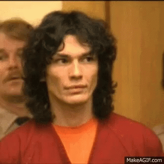 A Man With Long Hair Is Wearing A Red Jacket And An Orange Shirt . GIF
