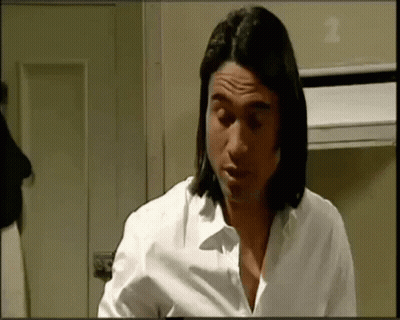 A Man With Long Hair Is Wearing A White Shirt And Looking Down . GIF