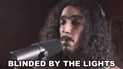 A Man With Long Hair Singing Into A Microphone With The Words Blinded By The Lights Below Him GIF