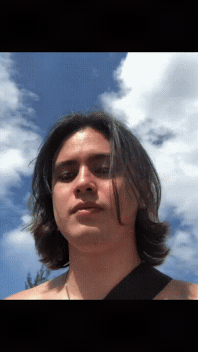 A Man With Long Hair Stands In Front Of A Blue Sky With Clouds GIF
