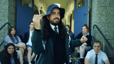 A Man With Long Hair Wearing A Blue Hat Stands In Front Of A Group Of Students GIF
