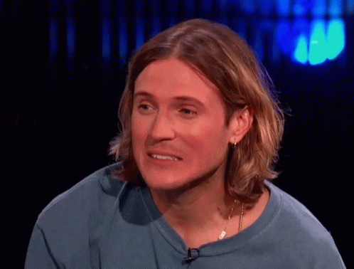 A Man With Long Hair Wearing A Blue Shirt And Earrings GIF