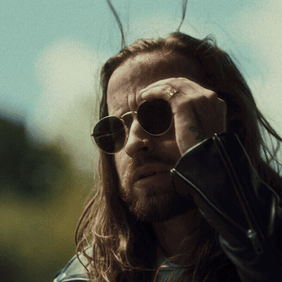 A Man With Long Hair Wearing Sunglasses Has A Tattoo On His Arm GIF