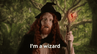 A Man With Long Red Hair Is Dressed As A Wizard And Holding A Wand . GIF
