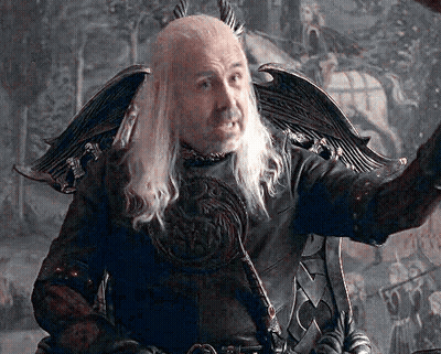A Man With Long White Hair And A Beard Is Sitting In A Chair With His Arm Outstretched GIF