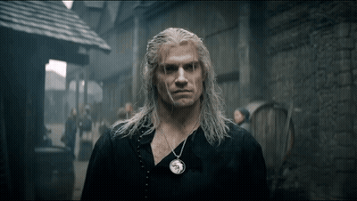 A Man With Long White Hair And A Necklace On His Neck Is Standing In Front Of A Brick Building . GIF